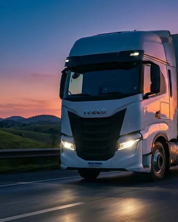 Carreta Iveco S-Way da PRA LOG em rodovia BR ao anoitecer com morros e céu rosa-laranja ao fundo